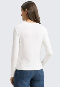 Witte lange mouwen top van ribstof met een ronde halslijn en een rechte zoom, gecombineerd met donkerblauwe jeans.