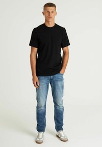 Crna pamučna majica s okruglim izrezom, uparena s svijetlopčelim trapericama. Model nosi sive tenisice s bijelim naglascima.