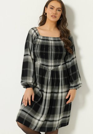 Vestido de cuadros en blanco y negro con escote cuadrado, mangas largas y cintura fruncida. La tela tiene una textura suave y una silueta fluida.