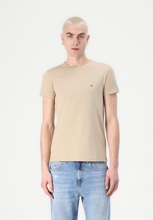 Beige bomull T-skjorte med rund hals, korte ermer, og en liten logo på brystet, kombinert med lyseblå denimjeans.