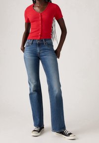 Haut rouge côtelé à manches courtes avec boutons ; jean droit bleu ; baskets noires et blanches. Texture lisse, coupe décontractée.