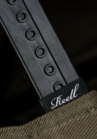 Black plastic strap featuring round cutouts, attached to a textured fabric in olive green with a black label reading "Reell."