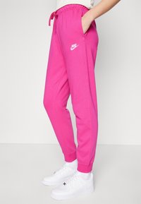 Pink sweatpants with an elastic waistband and drawstring, featuring side pockets and a white Nike logo on the left thigh.