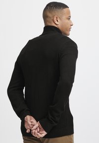 Schwarzer Rollkragenpullover mit strukturiertem Design und gerippten Bündchen, mit einer figurnahen Silhouette und einer glatten Strickoberfläche.