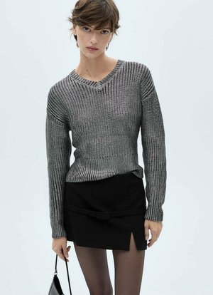 Maglione grigio lavorato a maglia con scollo a V, maniche lunghe e texture a coste, abbinato a una mini gonna nera con uno spacco laterale e dettaglio cintura.