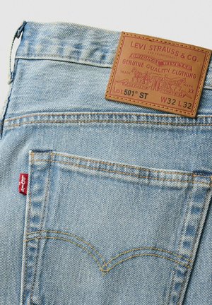 Lyseblå denim jeans med en læderlap med branding, orange syninger og et rødt mærke på baglommen. Klassiske designelementer.