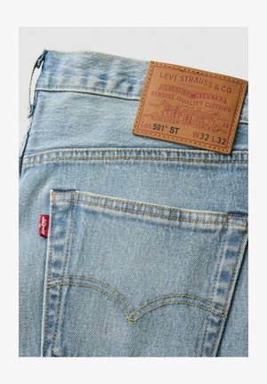 Lyseblå denim jeans med en læderlap med branding, orange syninger og et rødt mærke på baglommen. Klassiske designelementer.