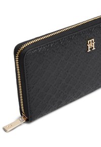 Μαύρο πορτοφόλι με φερμουάρ κατασκευασμένο από υλικό συνθετικής υφής, με φερμουάρ σε χρυσό τόνο και ανάγλυφο λογότυπο στην επιφάνεια.