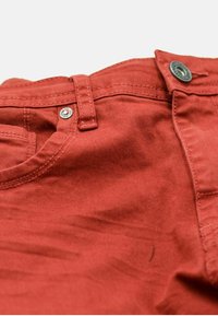 Pantalones de algodón rojos con una textura suave, que cuentan con un cierre de botón metálico y bolsillos cosidos, realzados por sutiles detalles de pliegue.