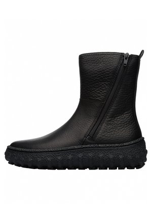 Bottine en cuir noir texturé avec semelle épaisse et robuste et fermeture éclair latérale sur fond blanc.