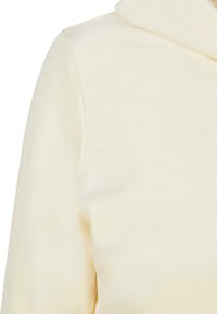 Un hoodie de couleur crème fabriqué en tissu doux avec une texture lisse, présentant une capuche structurée et des détails de couture subtils.