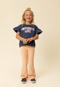 Donkerblauwe korte mouw sweatshirt met de tekst "UNIVERSITY LOVE" in roze; gecombineerd met licht perzikkleurige corduroy uitlopende broek en donkerblauwe schoenen.