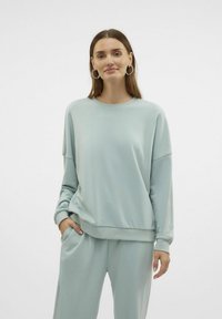 Lyseblå sweatshirt lavet af blødt stof, med afslappet fit, rund hals og sænkede skuldre, parret med matchende bukser.