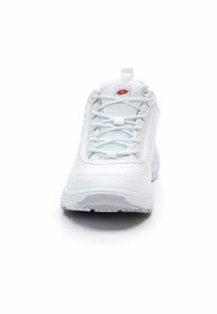 Scarpa sportiva bianca con tomaia in pelle testurizzata, inserti in mesh e design con lacci; presenta un logo rosso ben visibile sulla linguetta.