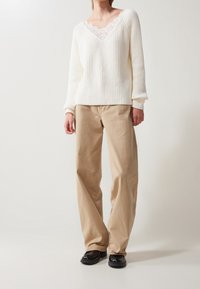 Krémový pletený svetr s krajkovým lemováním výstřihu, doplněný o světle béžové kalhoty s širokými nohavicemi a černé boty. Jemná textura, volný střih.