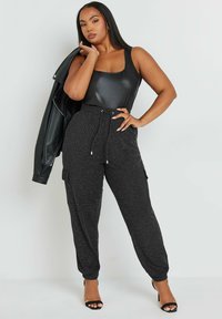 Svart bodysuit med fyrkantig halsringning, parat med texturerade svarta cargobyxor med fållade anklar och dragsko i midjan. Svart läderjacka.