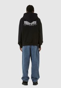 Felpa nera con un grande motivo floreale bianco sul retro, abbinata a jeans baggy blu e calzature nere.