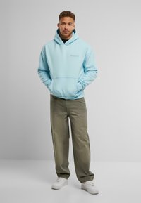 Lichtblauwe pullover hoodie met een voorzak en geribbelde manchetten, gecombineerd met losse olijfgroene broek en witte sneakers.