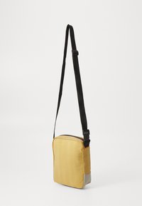 Gul nylon crossover-veske med grå bunn, rektangulær form, glidelås-lukking og justerbar svart stropp. Teksturert overflate.