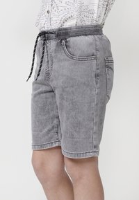 Pantalones cortos de mezclilla gris con cintura elástica, cordón negro y bolsillos frontales. La textura está ligeramente desgastada para un aspecto usado.