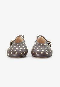 Chaussures en cuir marron avec un bout arrondi, des côtés découpés et des clous dorés partout. Bride ajustable avec un détail de boucle métallique.