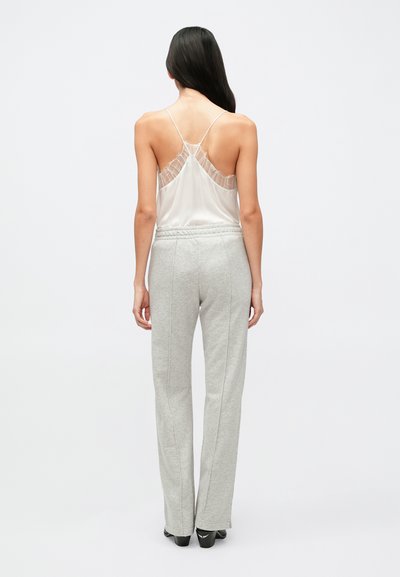 Ľahké biele tielko s priesvitným detailom na chrbte, spojené so sivými teplákmi s voľným strihom a elastickým pásom.