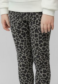 Grijze legging met luipaardprint en zwarte vlekken, voorzien van een strakke pasvorm en zachte textuur, gedragen met een lichtkleurige trui.