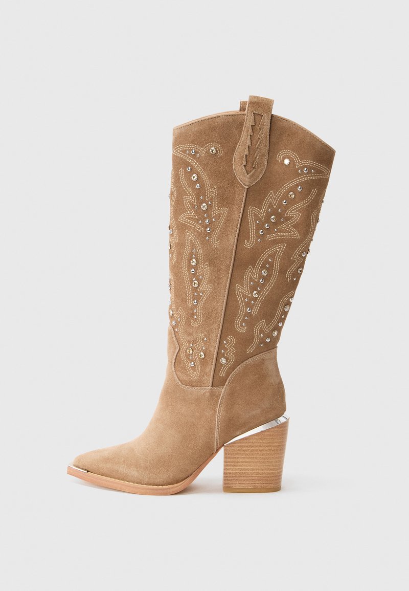 Botte western mi-mollet en suède beige avec broderies décoratives, ornements en strass, languette de tirage, bout pointu et talon empilé.