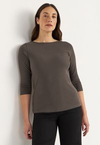 Grijze geribbelde langekatoenen top met een brede bootnek, gecombineerd met zwarte broek. Glad oppervlak en aansluitend ontwerp, zonder zichtbare patronen.