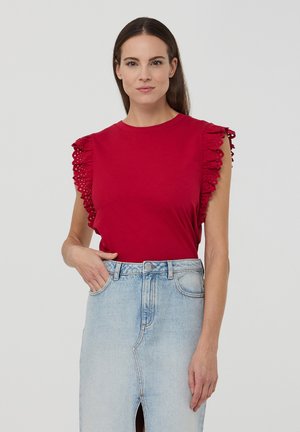 Maglietta di cotone rossa con maniche in pizzo arricciate, abbinata a una gonna di jeans azzurri a vita alta con spacco davanti e chiusura a bottoni.