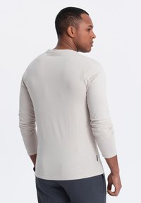 Beige Langarmhemd aus weichem Material mit rundem Ausschnitt und taillierten Ärmeln, das ein minimalistisches Design ohne sichtbare Muster aufweist.