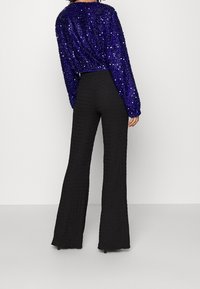 Top lungo a maniche larghe color viola con paillettes abbinato a pantaloni neri a palazzo con texture. L'outfit presenta un design corto con una vita aderente.