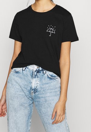 Musta puuvillapaita, jossa on pieni valkoinen sateenvarjokuva ja sadepisaroita, yhdistettynä haalistuneisiin korkeavyötäröisiin sinisiin farkkuihin.