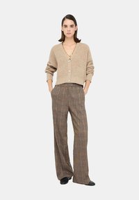Cardigan lavorato a maglia beige con design cropped e chiusura con bottoni, abbinato a pantaloni a gamba larga e alta vita in un motivo a quadri nero e beige.
