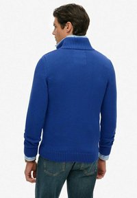 Blauwe gebreide trui met een hoge geribde kraag, geribde manchetten en zoom, gedragen over een licht overhemd, met een comfortabele pasvorm en een gladde textuur.