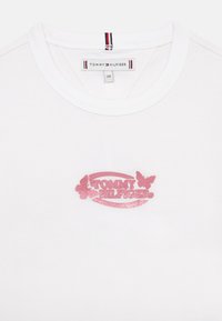 Vit bomull T-shirt med en rosa glittrig logotyp med fjärilsdetaljer, rund halsringning och en etikett märkta "TOMMY HILFIGER."