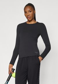 Melnas garām piedurknēm sporta topiņš ar apaļu kaklu un pieguļošu dizainu. Iezīmēts ar diskrētāku logo apakšmalā un mīkstu, gludu auduma struktūru.