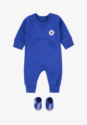 Kék csecsemő kezeslábas zsebbel, bordás mandzsettákkal és kerek nyakkal; hozzá illő kék cipőcske, amely fehér fűzőket utánoz.
