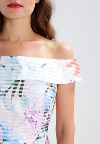 Sukienka na ramiączkach wykonana z lekkiego materiału, z pastelowym kwiatowym wzorem oraz subtelnymi poziomymi paskami w odcieniach niebieskiego, różowego i zielonego.