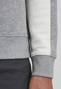 Grå sweatshirt med detaljer i hvid stribe, ribbede manchetter og kant, der showcases en blød tekstur og afslappet design.