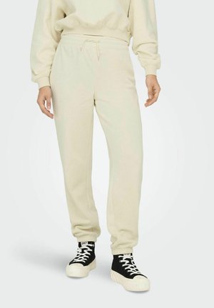 Beige sweatpants met een elastische tailleband en boorden, gemaakt van zachte stof. Gecombineerd met zwarte hoge sneakers met witte veters en zool.