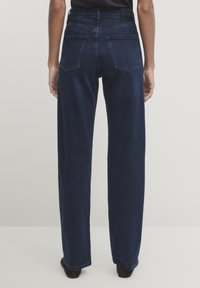 Jeans ampi, di colore blu scuro, con vita alta. Presentano due tasche posteriori e una texture liscia, realizzati in tessuto denim.