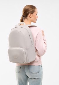 Szürke hátizsák lekerekített formával, párnázott pántokkal és egy elülső cipzáras zsebből áll. Az anyaga textúrált és tartós.