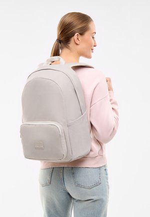 Šedý batoh s zaobleným designem, polstrovanými popruhy a přední kapsou na zip. Materiál vypadá texturovaně a odolně.