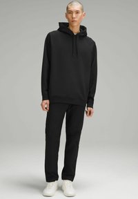Sudadera con capucha negra y mangas raglán, combinada con pantalones negros a juego y zapatillas blancas. Diseño simple, textura suave.