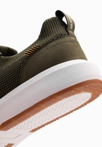 Zapatilla de malla verde con un diseño elegante, que presenta una entresuela blanca, una parte superior de olivo texturizada y una suela de goma con un agarre con patrón.