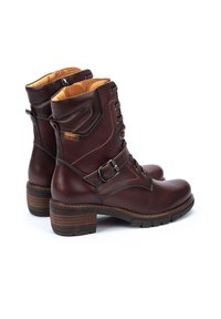 Brown leather ankle boots with lace-up front, side zipper, and buckle detail. Stacked heel and textured sole for stability.