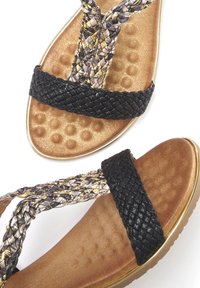 Schwarze geflochtene Riemen kreuzen sich über einem strukturierten goldenen Fußbett mit glatter Oberfläche und abgerundeten Kanten, was ein lässiges Sandalendesign bietet.