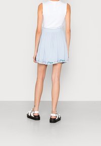 Jasnoniebieska spódnica z miękkiego materiału, z elastycznym pasem. Posiada kwiatowe hafty wzdłuż dołu. W zestawie z białymi sandałami.