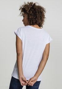 T-shirt blanc à manches courtes avec une coupe décontractée, encolure ronde et manches retroussées, associé à un jean bleu. Pas de motifs ni d'accents marquants.